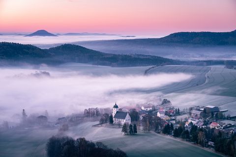 Sonnenaufgang über bewaldeten Hügeln von Papstdorf, klarer Himmel.
