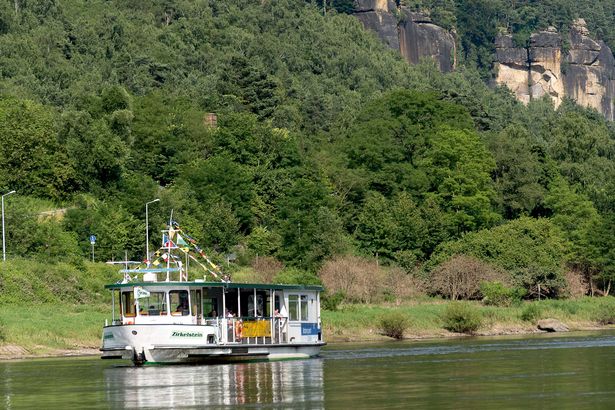 Fähre auf Elbe, grüne Hügel, Felsen, blauer Himmel im Hintergrund.