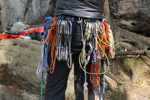 Person mit Kletterseilen und Karabinern an Gürtel.